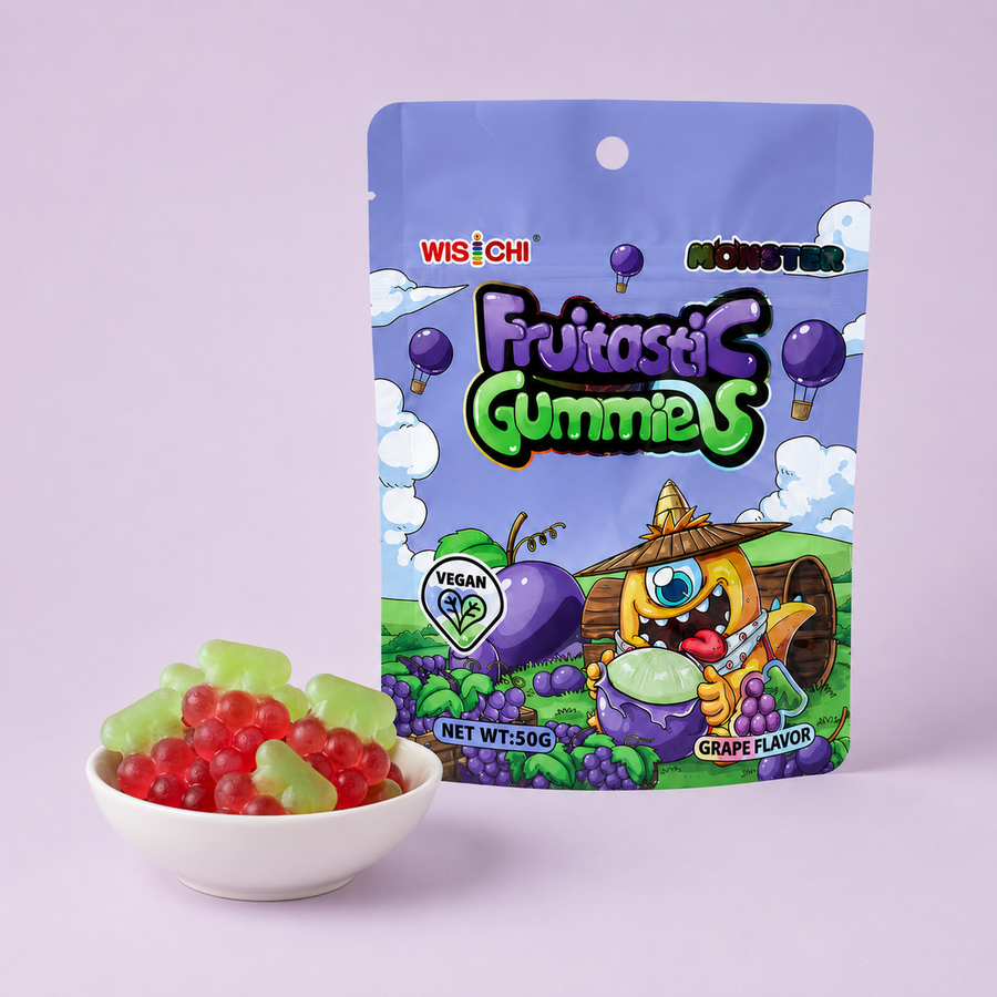 A bag of Wisichi Monster Fritastic Gummies grape flavor is shown next to a small white bowl filled with red and green gummy candies, set against a solid light purple background.
