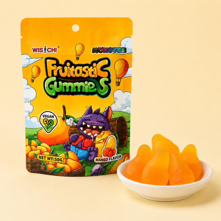 A bag of Wisichi Monster Fruitasi Gummies, Mango Flavor, shown next to a small white bowl filled with orange-yellow gummy candies on a light beige background.
