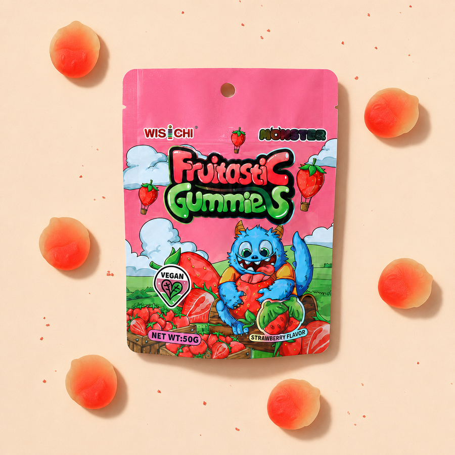 A package of Wisichi Fruitasi Gummies, strawberry flavor, featuring a pink stand-up pouch with a cartoon monster character and illustrations of strawberries. The package is centered on a light peach background decorated with scattered peach-shaped gummies.