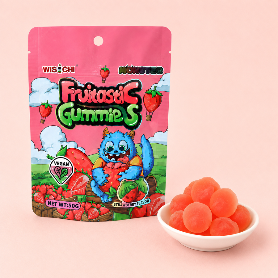 A pink stand-up pouch of Wisichi Monster Fruitasi Gummies, shown next to a small white bowl filled with round, translucent orange-red gummy candies on a solid pale pink background.