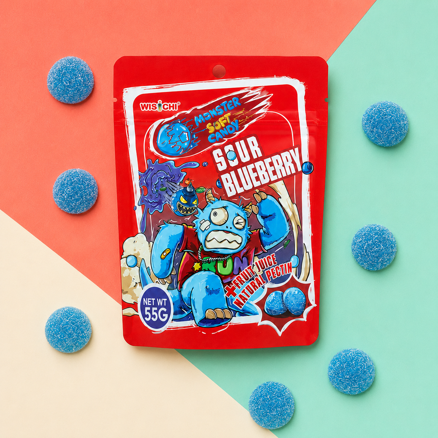 A package of Wischi Monster Candy Sour Blueberry candy is displayed on a diagonally split coral, cream, and mint green background, surrounded by scattered blue sugar-coated gummy candies.