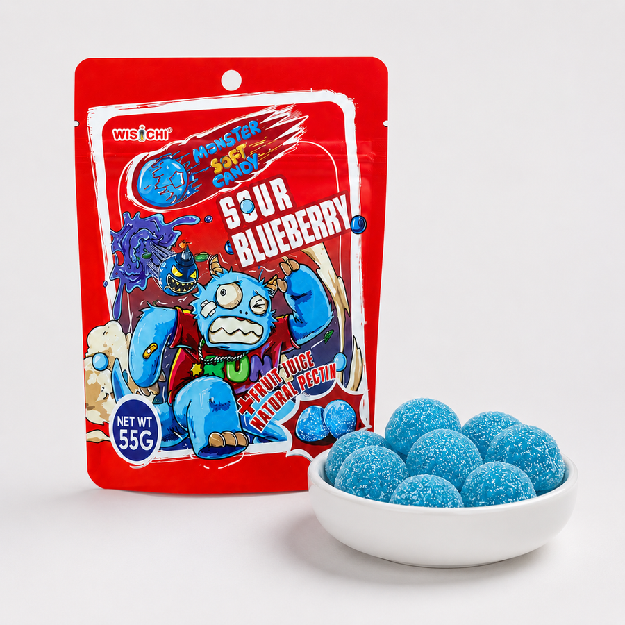 A red bag of Wischt Monster Candy Sour Blueberry candy stands next to a small white bowl filled with round blue candy pearls on a light gray background.